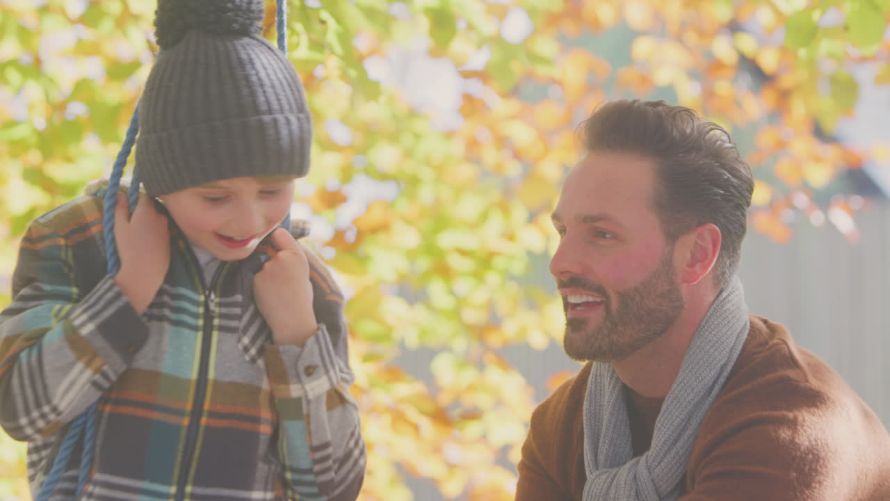 padre empujando hijo divirtiéndose en el columpio de cuerda en el jardín de otoño