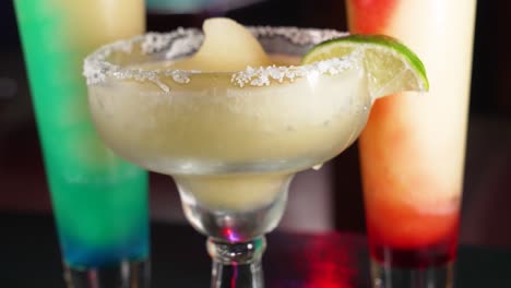 frosty frozen margarita dressed with salt rim and lime wedge upstages two swirl margaritas behind, close up 4k