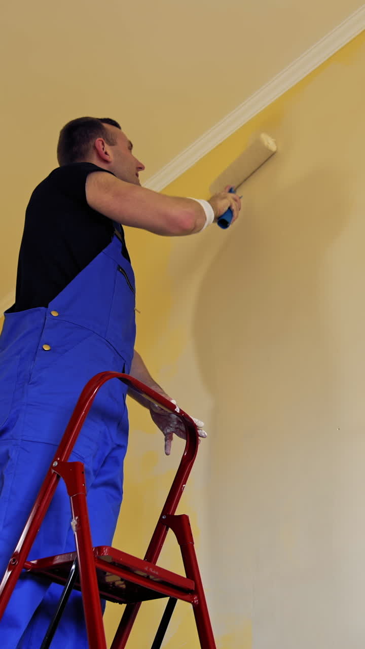 Man painting a yellow wall with a roller at work. Offering professional painting services. Vertical video