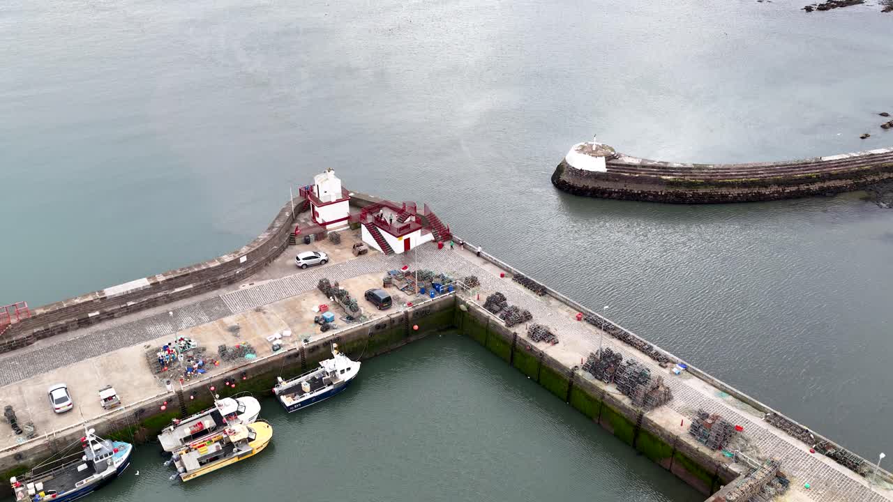 Drone camera ascends over Dundee harbor, revealing boats, lighthouse, pier, and calm coastal waters