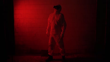 Red-smoke-shot-worker-in-respirator-and-protection-suit-standing-against-brick-wall