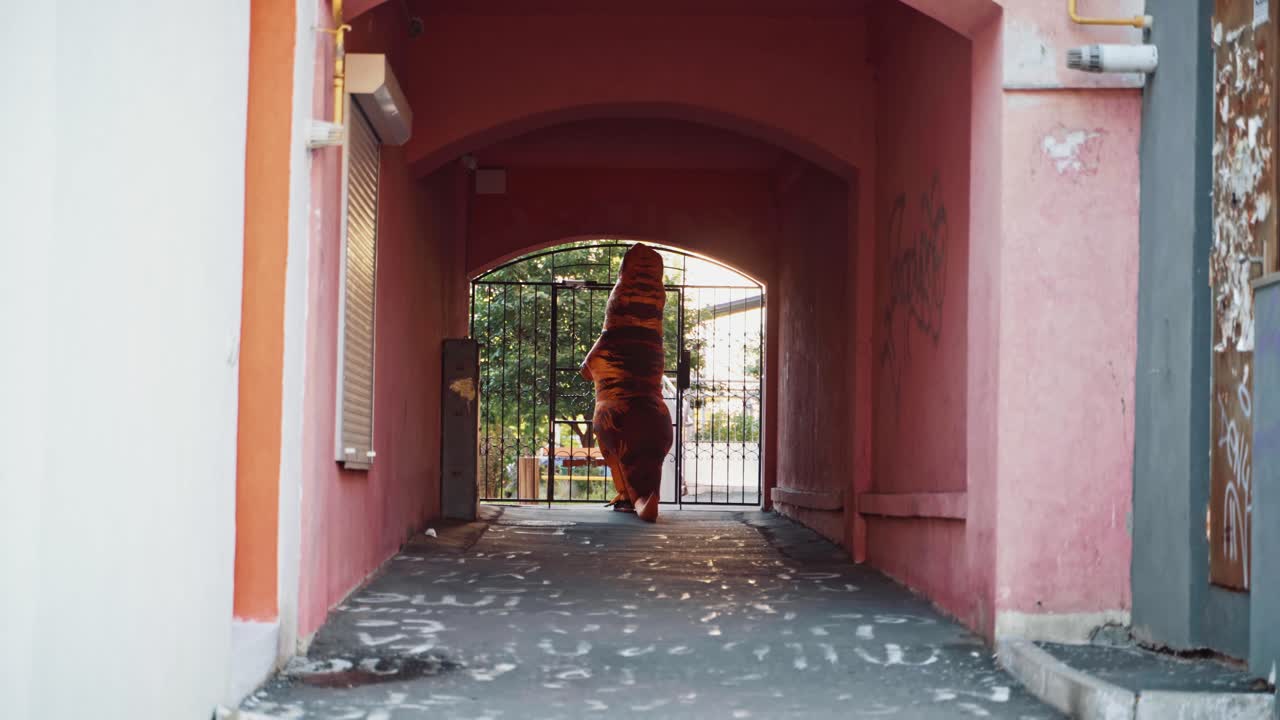 Dinosaur walking in alley. Dinosaur costume in alley behind metal bars at city street