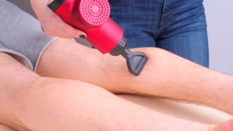 masajista femenina masajeando los músculos de la pantorrilla de un deportista con un masajeador de percusión