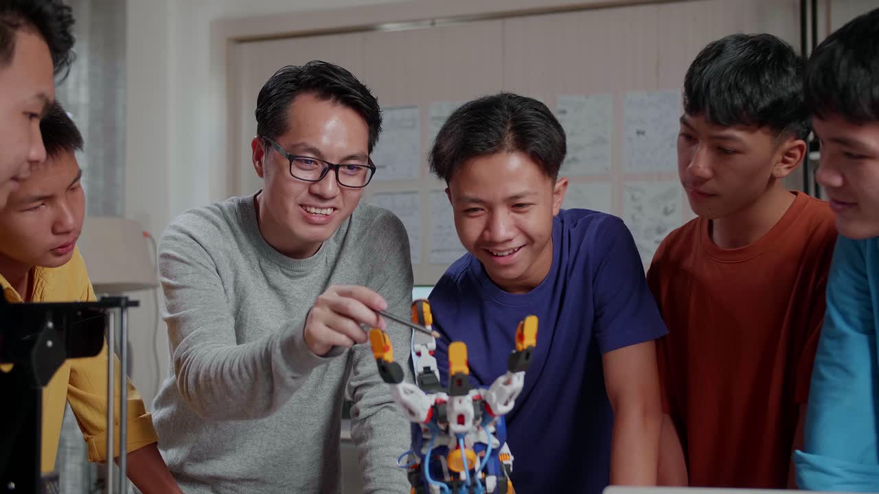노트북과 3d 프린팅을 가진 아시아 남자가 학교에서 소년들에게 사이보그 손을 사용하는 방법을 설명합니다.