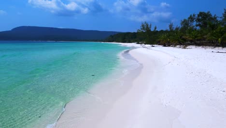 sok san beach with turquoise water washing the white sand, surrounded by palm trees and tropical vegetation. smooth aerial view flight