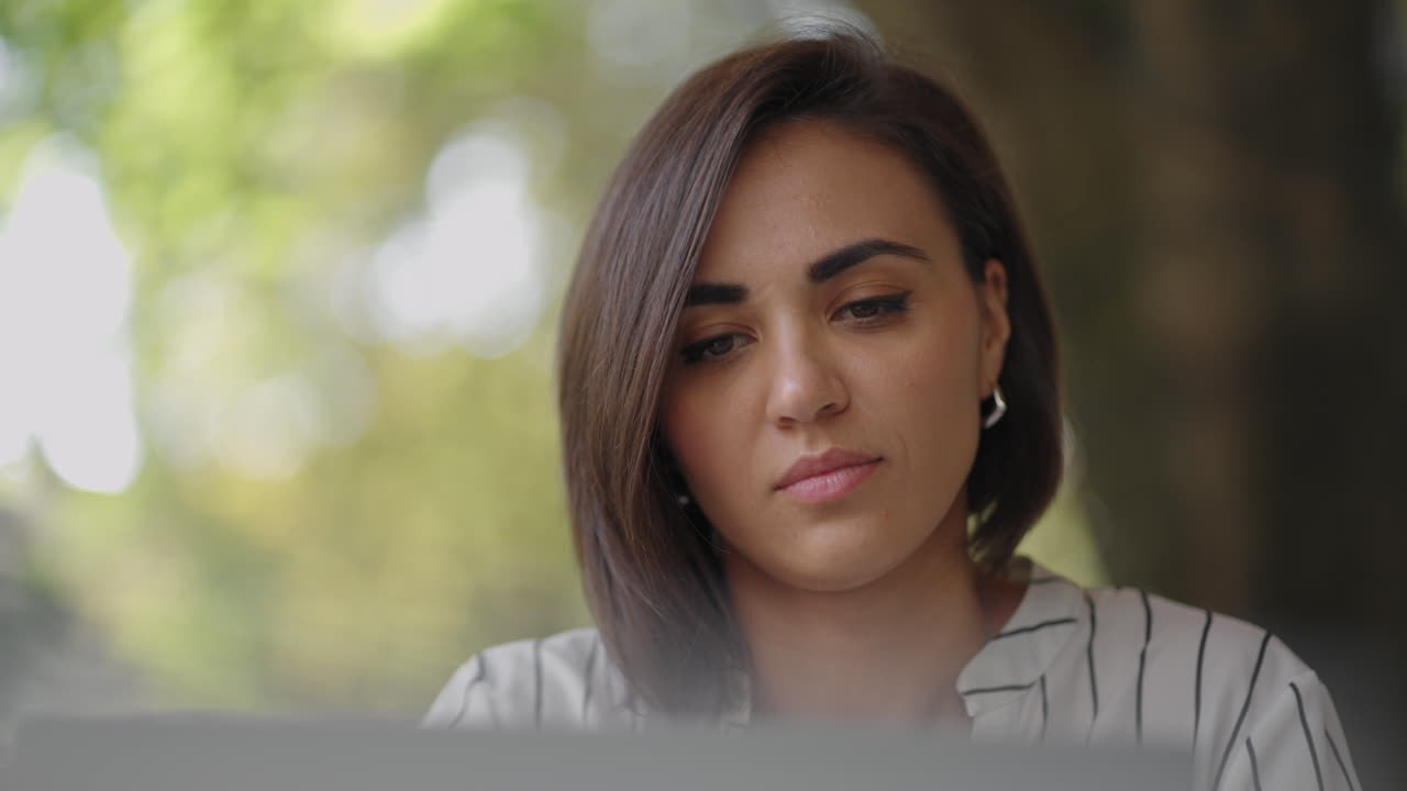 retrato mujer grave morena grupo étnico hispano se sienta en una mesa en un café de verano con una computadora portátil. escribe en el teclado y se somete a capacitación en línea compra y trata con un banco en internet