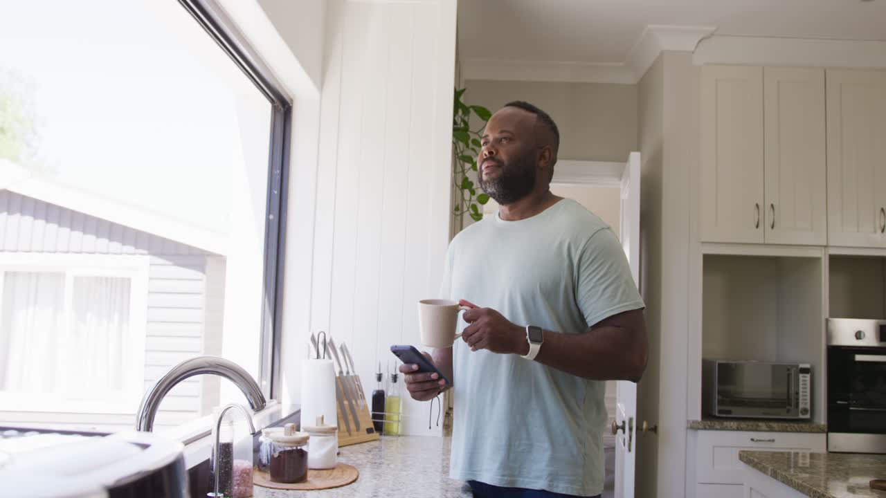 Starting routine African American man grabbing mug in kitchen holding mug and checking phone
