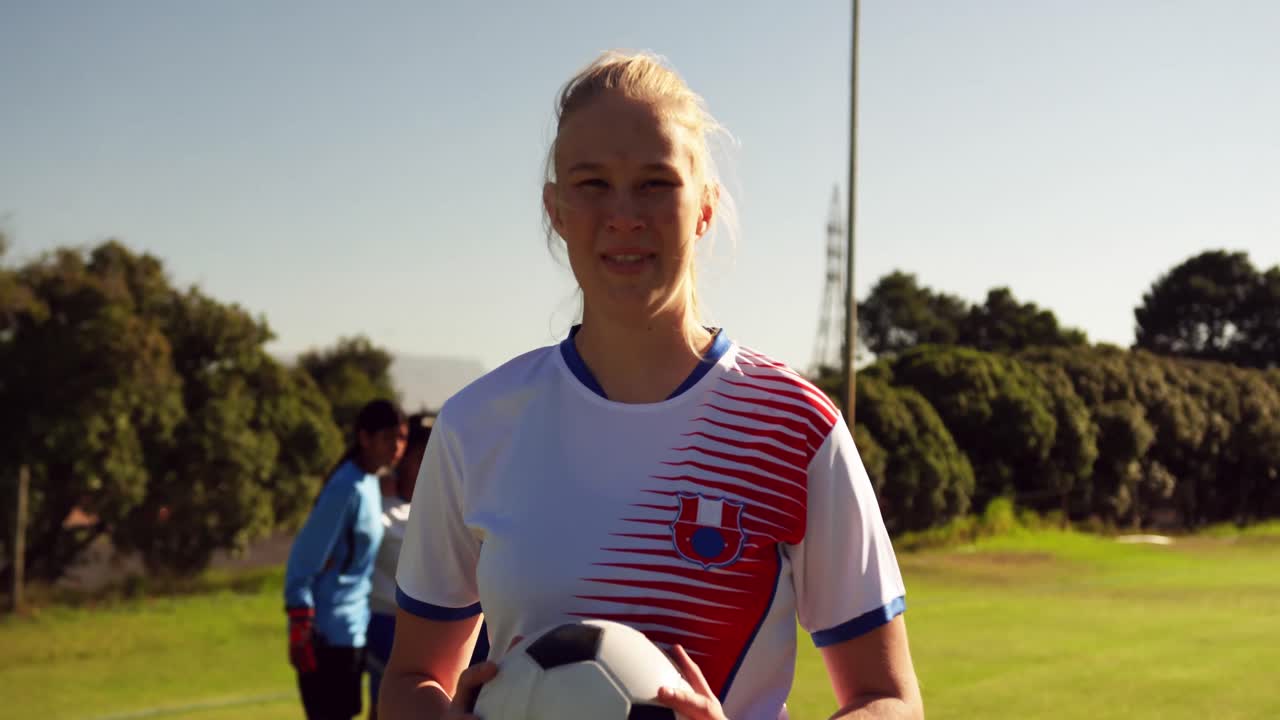 여자 축구 선수 는 팀 동료 들 이 축구장 에 서 있는 동안 공 을 들고 있다. 4k