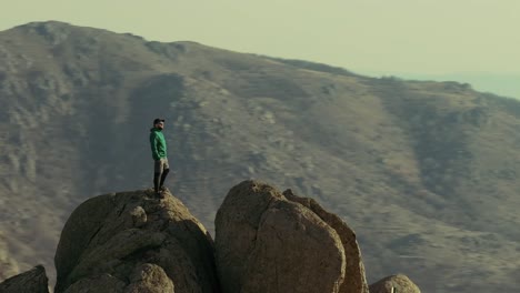 Un-Excursionista-Solitario-Se-Encuentra-En-La-Cima-De-Una-Montaña-Con-Un-Disparo-Rápido-De-Un-Dron-De-Paralaje