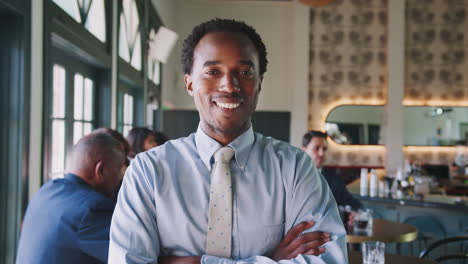 portrait of smiling businessman in busy cocktail bar of restaurant with customers in background