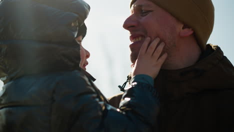 a father carrying his son, the boy is playing with his chin, with light reflection behind the boy and electric pole in the background