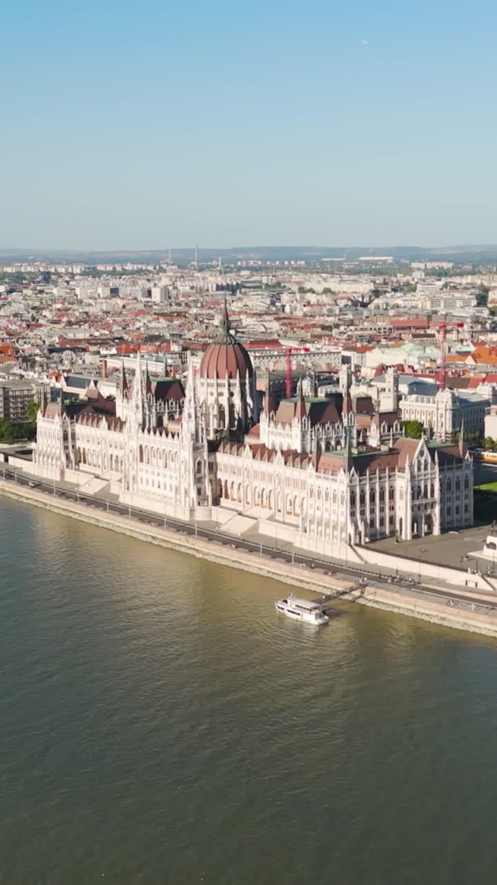 Il Parlamento ungherese si erge fiero lungo il fiume Danubio sotto un cielo limpido. Video aereo verticale