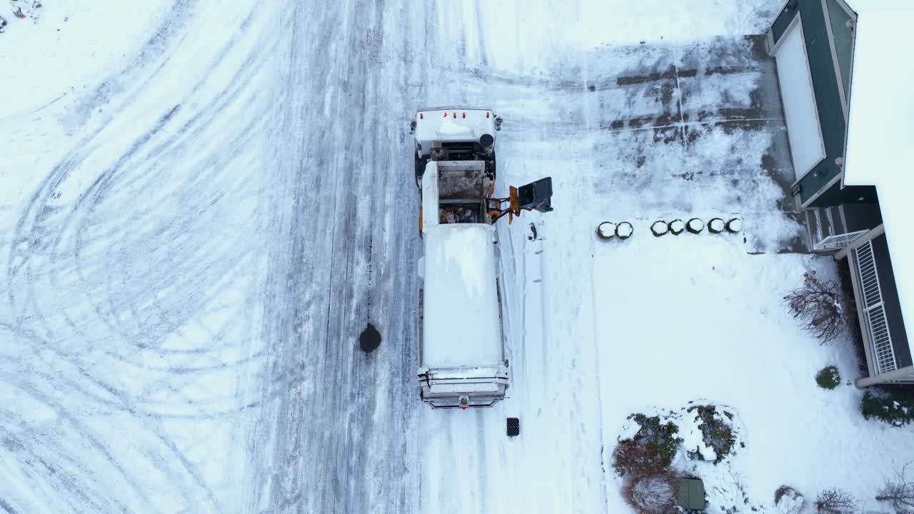 Top down drone shot of a city dump truck picking up trash with snow covered roads