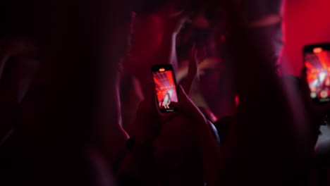 concert crowd with raised hands and smartphones capturing performance in vibrant lighting atmosphere