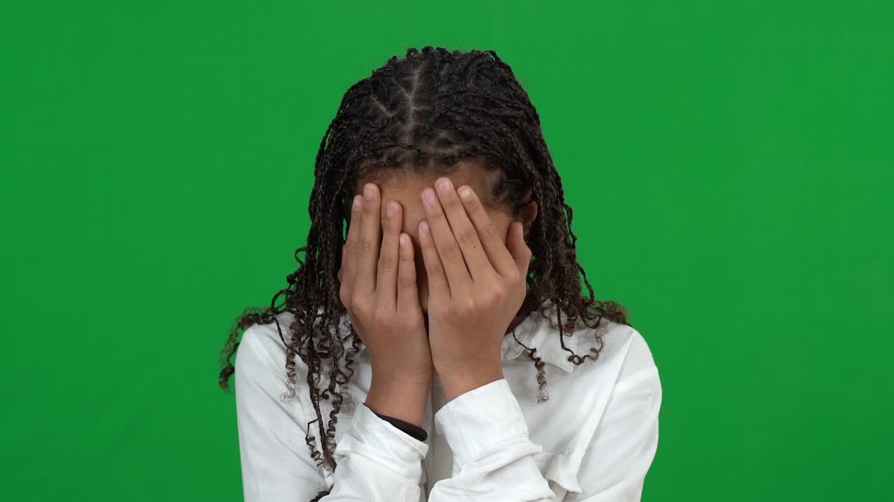 Close-up of scared teenage girl closing face with hands looking at camera shaking head no at chromakey background. Portrait of frightened African American teenager on green screen.
