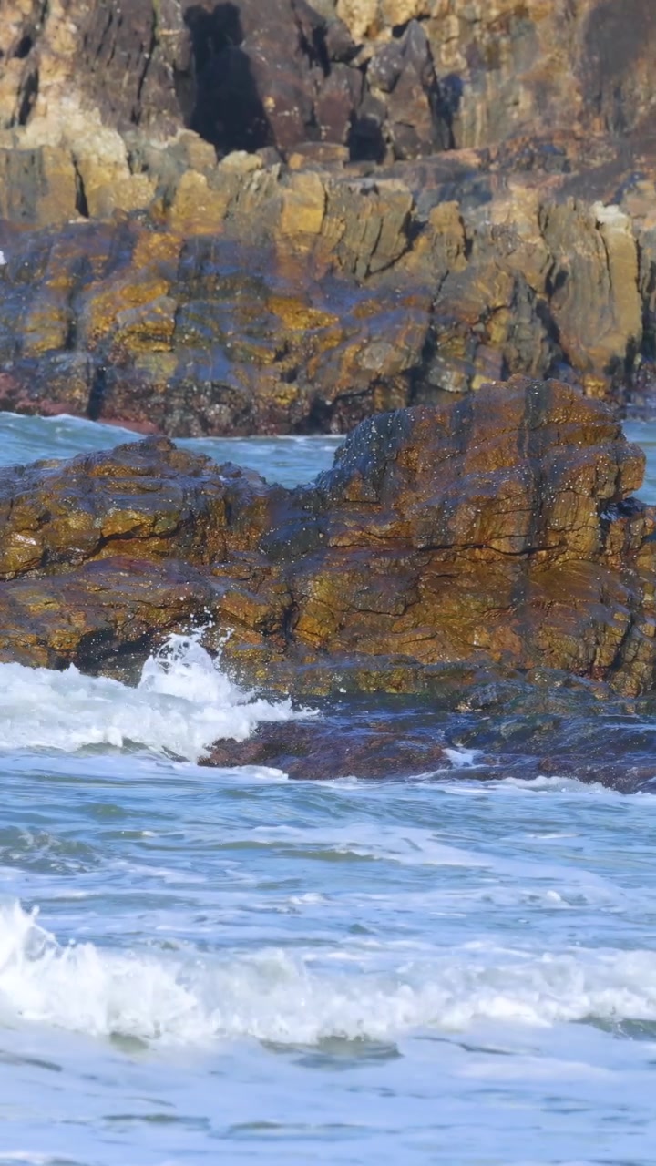 Dinamiche onde oceaniche si infrangono contro rocce frastagliate sotto la luce del giorno, catturando la potenza e la bellezza della natura.