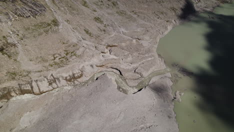 Small-water-stream-flowing-through-the-mountains-into-the-glacier-lake,-Drone-shot