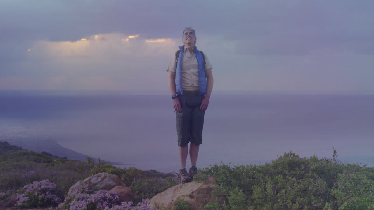 Man standing on rocky coastal cliff overlooking ocean at dusk, showing animated tech icons and data