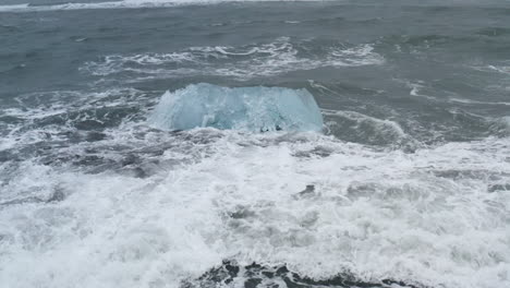 stunning drone shot of waves breaking on a beautiful ice rock at diamond beach in iceland