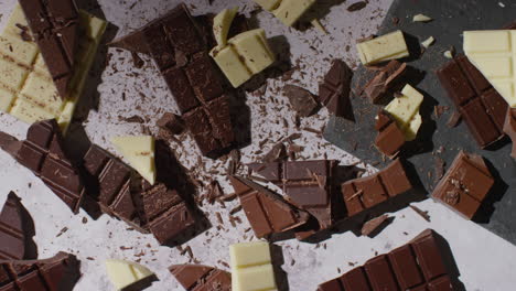 grated chocolate being dropped on broken bars of milk plain and white chocolate