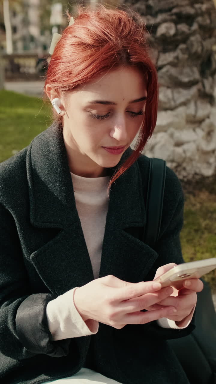 Giovane donna dai capelli rossi che usa lo smartphone e gli auricolari all'aperto