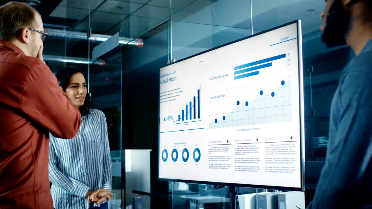 un equipo diverso de trabajadores empresariales en la sala de conferencias tienen una discusión sobre estadísticas y gráficos mostrados en una presentación de televisión.