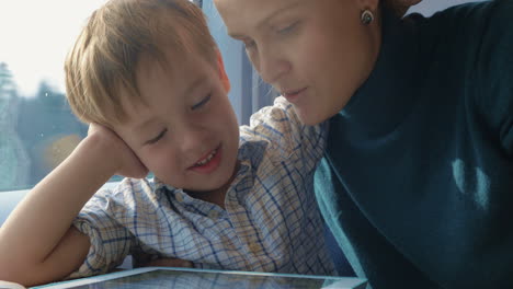 mother and son playing game on pad in train