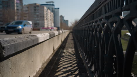 vista cercana de una carretera urbana con vehículos en movimiento en el fondo, se centra en la barrera de la carretera con sombras proyectadas por la barandilla