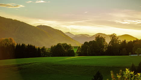 a sunrise with a yellow glow over a green landscape with mountains and meadows