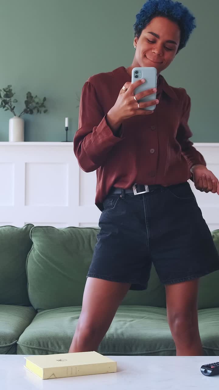 Young overjoyed african american woman jumps up from couch reading sms on phone