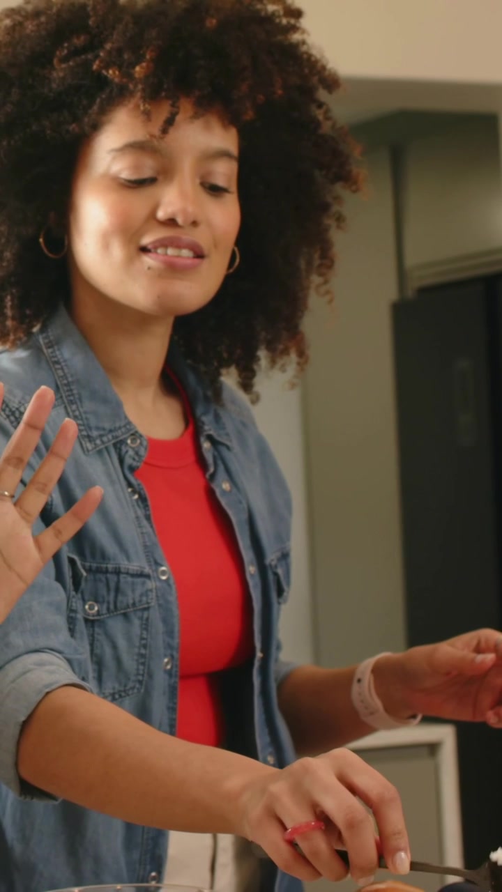 Video verticale: Una donna in denim cucina in cucina, disponendo l'avocado con le pinze, con gli ingredienti in primo piano.
