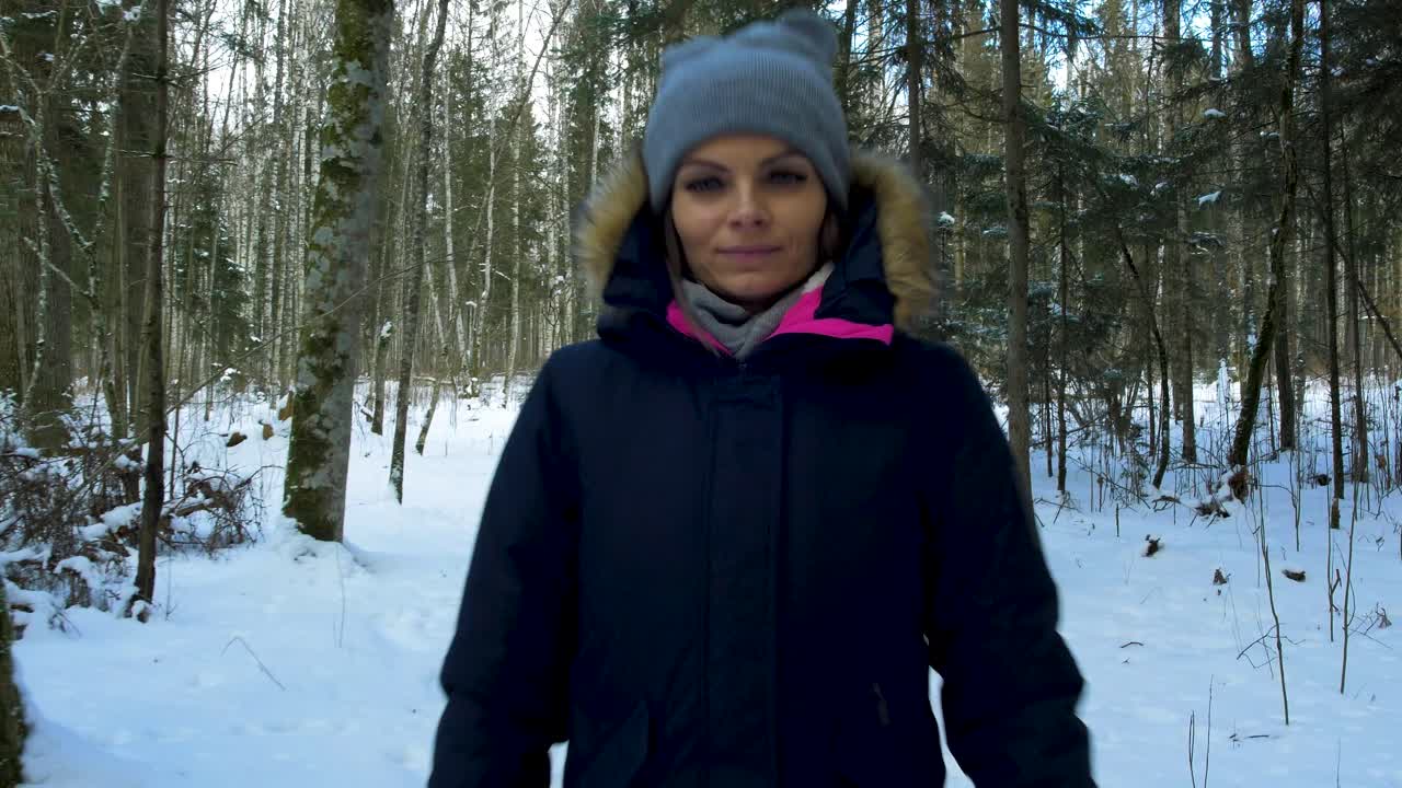 A young caucasian girl walking on winter forest trail in snow covered winter pine forest at sunny day, walk alone in frosty weather, push in gimbal shot, ending black at chest, walk towards camera