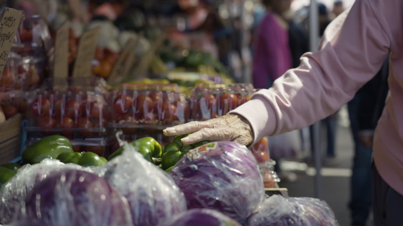 disparo en cámara lenta de una mano anciana tocando frutas y verduras frescas que se ofrecen en un mercado