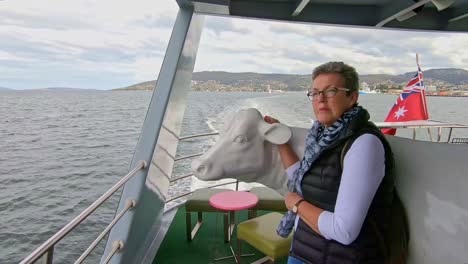 hobart, tasmania, australia - 13 march 2019: woman passenger admiring the view on a tourist boat leaning against a life-sized model of a cow