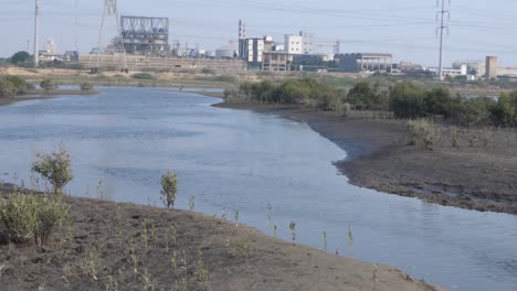 Wasserstraße,-Die-Durch-Das-Mangroven-Abholzungsgebiet-In-Karachi-Verläuft,-Mit-Fabrik-Im-Hintergrund