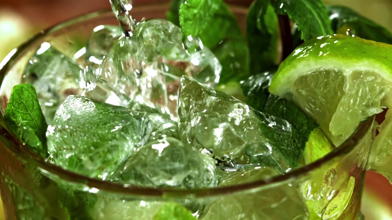 Lähikuva, jossa vettä kaadetaan tuoreeseen mojitoon jäiden ja mintun kera.