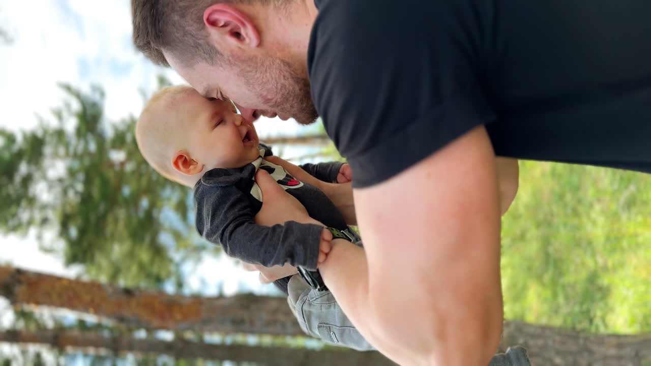 Bearded Caucasian man holding a tiny baby in the forest. Happy dad kisses his newborn son. Vertical screen.