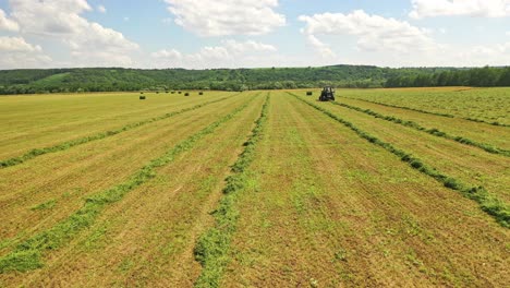 Low flight over the green field near tractor in summer. Agricultural tractor working on the grassland on the field in the countryside.