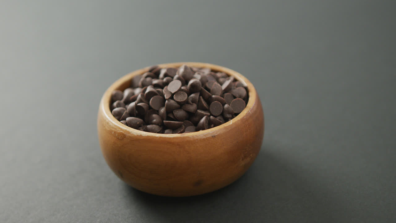 Video of wooden bowl of chocolate chip over grey background