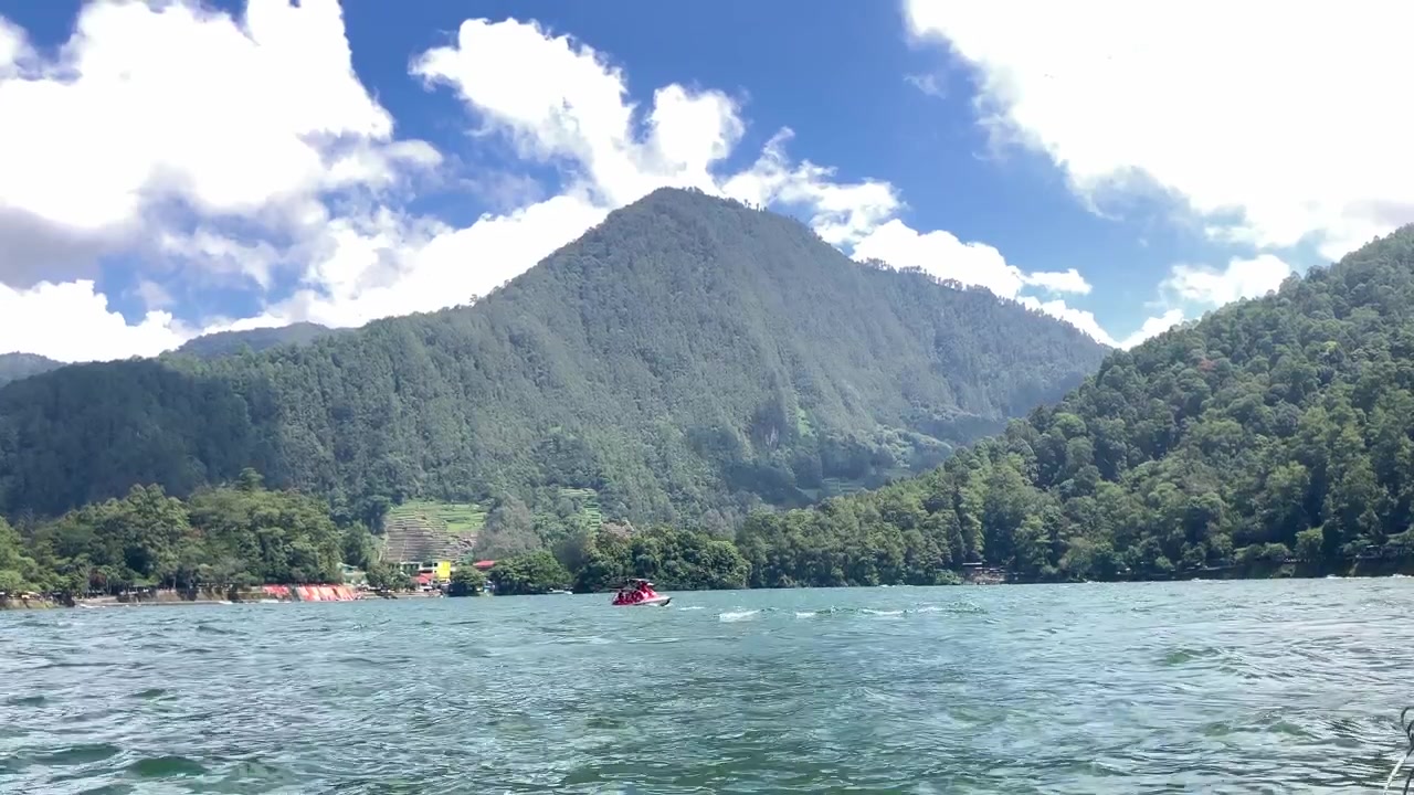 Yemyeşil dağlar ve beyaz bulutlarla çevrili sakin bir gölü geçen bir teknenin güzel 4K editoryal görüntüleri. Seyahat ve doğa belgeselleri için mükemmel.