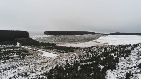 Long-road-reveal-aerial-into-distance-across-highland-snowy-countryside-moors-rising-pan-right