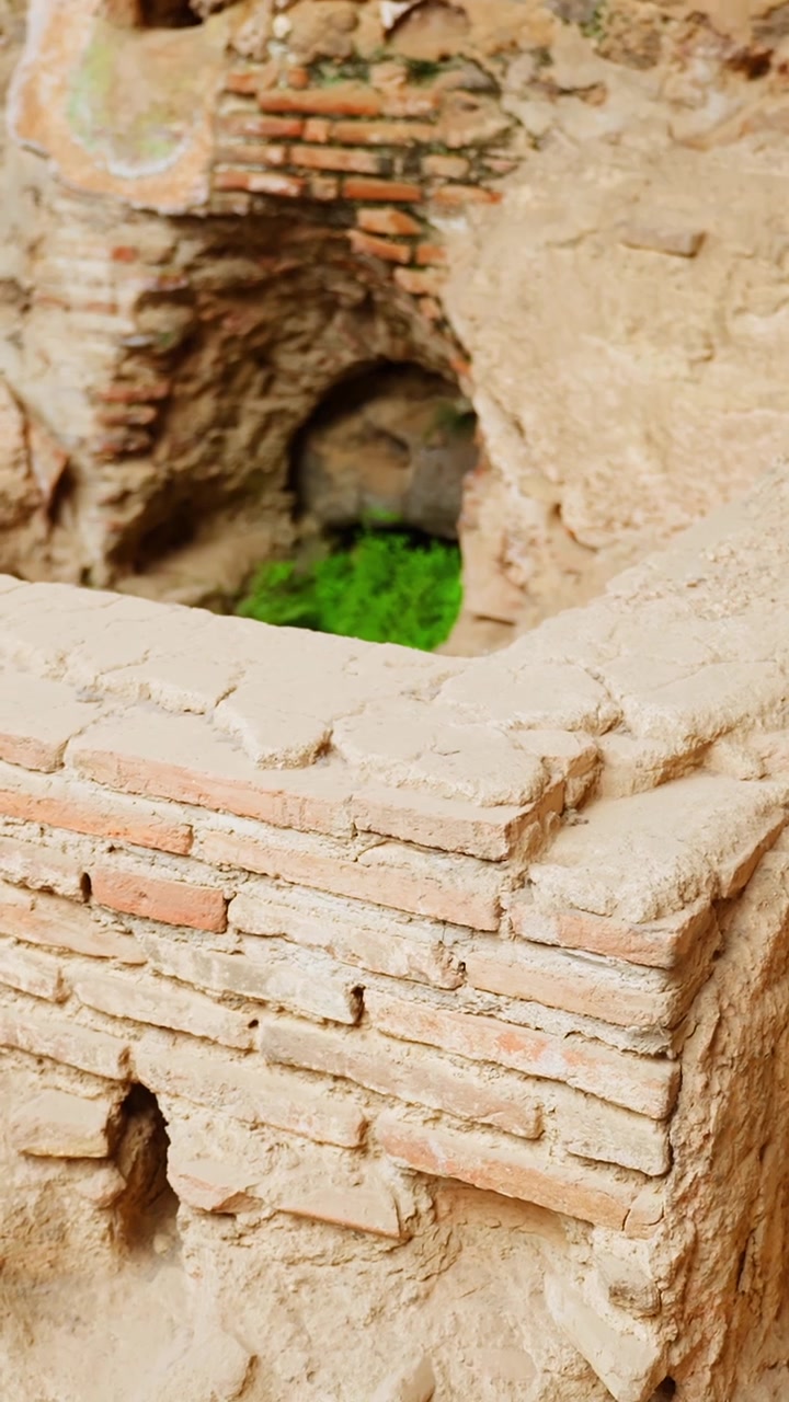 Primer plano vertical de soportes de ladrillo excavados y paredes de yeso erosionadas en Pompeya, revelando frágiles detalles de construcción romana dentro del antiguo sitio arqueológico.