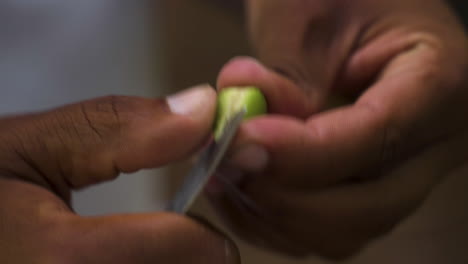 manos negras pelando semillas de café verde frescas con un cuchillo, de cerca