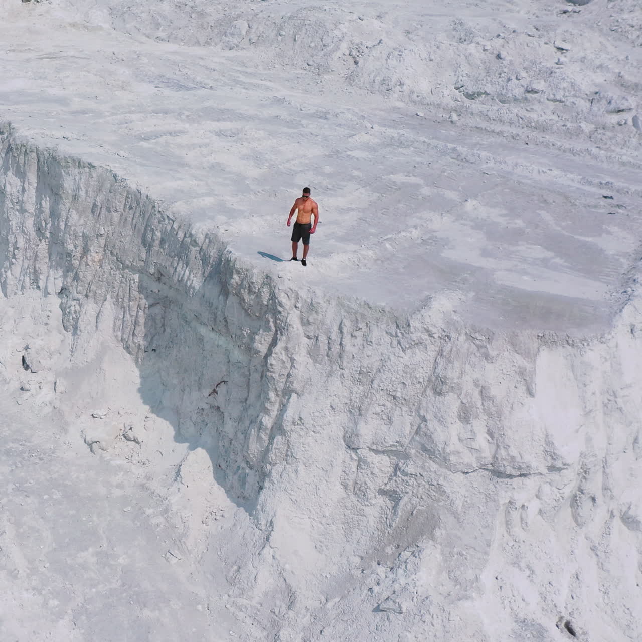 Sportsman on a white canyon. Healthy man in shorts doing his daily training outdoors. Strong athlete runs on the rocky hill in a sunny summer day. Aerial view.