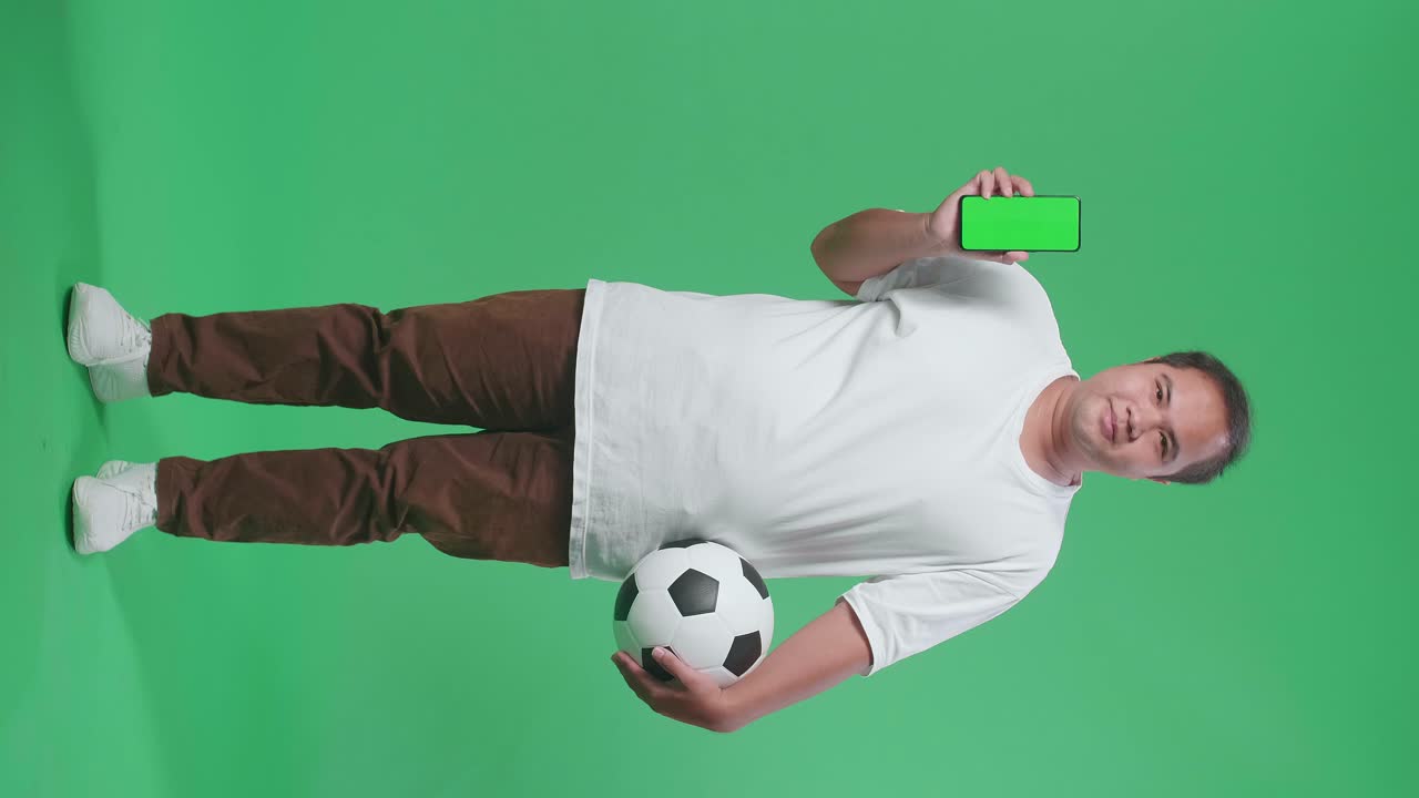 hombre con una pelota de fútbol y un teléfono inteligente en un fondo de pantalla verde