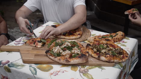 chef cuts slices of pizza and gives to people sitting at the table