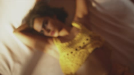 chica morena con labios rojos y ropa amarilla acostada y mirando hacia la cámara
