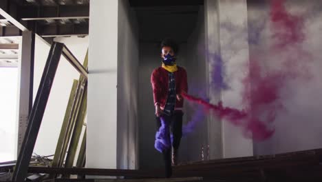 mixed race man holding blue and purple flares walking through an empty building