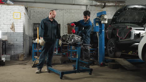 two engineers in an automotive workshop, one wearing red gloves working on a car engine while the colleague observes, background features parked cars, mechanical tools, and various equipment