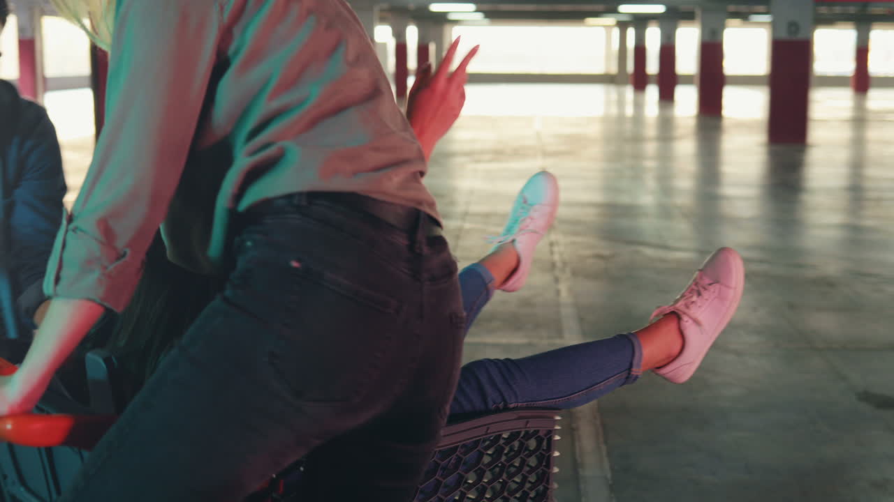 joven grupo de alegres amigos caucásicos divirtiéndose en un estacionamiento vacío con un carrito de supermercado